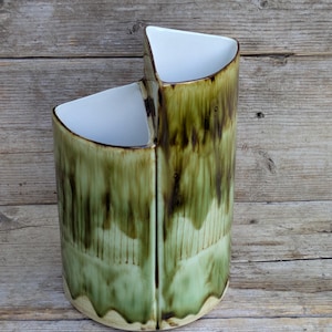 May include: A ceramic vase featuring a two-tiered, stepped design with a white interior and a glossy exterior glaze in shades of olive green and dark brown. The exterior surface displays a vertical drip pattern with a smooth, reflective finish.