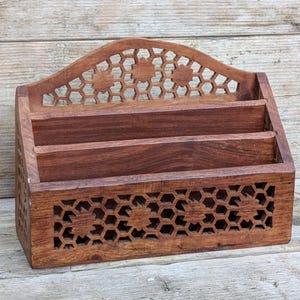 May include: A brown wooden letter holder featuring two tiers for storage. The front panel and the arched top piece are decorated with a laser-cut honeycomb pattern interspersed with star-shaped cutouts. The sides also feature the same pattern.
