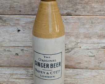 Puede incluir: Una botella de cerveza de jengibre de gres vintage con un acabado esmaltado bicolor en tonos tostado y blanco roto. El frente presenta una etiqueta impresa en negro que dice The Original Ginger Beer Batey & Co Ltd London. Tapa gris oscuro.