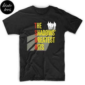 Può includere: T-shirt nera con la scritta "THE SHADOWS' GREATEST HITS" in rosso, giallo e bianco. Una silhouette bianca di una band è sopra la parola "SHADOWS". La maglietta ha un girocollo e maniche corte.