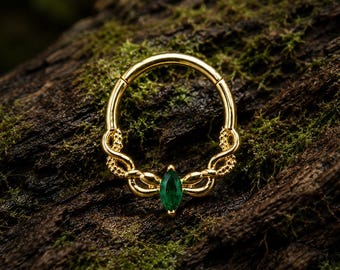 Pode incluir: Um anel circular de tom dourado com uma pedra preciosa verde-esmeralda em corte marquise na base. A banda metálica apresenta uma textura torcida, semelhante a uma corda, que envolve as laterais, conduzindo à cravação da pedra central.