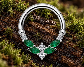 Pode incluir: Um anel de aro articulado em tom prateado com um segmento decorativo adornado com quatro pedras verdes de corte marquise e três pedras claras de corte brilhante redondo dispostas num padrão simétrico na curva inferior do aro.