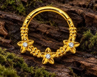 Pode incluir: Um anel de aro dourado com três motivos de flores de cinco pétalas, cada uma centrada com uma pequena pedra preciosa transparente. O anel é decorado com grupos de pequenas contas douradas ao longo da banda.