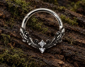 Pode incluir: Um anel circular de prata com um design ornamentado de filigrana de metal escurecido na metade inferior. A peça de joalharia é acentuada com duas pequenas pedras preciosas transparentes de corte redondo cravadas verticalmente no centro.
