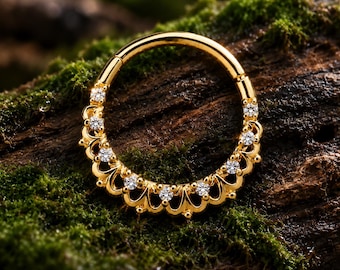 Puede incluir: Un anillo circular de oro con un segmento articulado y un borde festoneado decorativo en la mitad inferior. El diseño festoneado está acentuado con siete pequeñas piedras preciosas transparentes de corte redondo incrustadas en el marco.