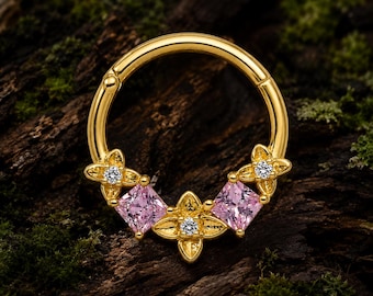 Pode incluir: Um anel de aro articulado em ouro com três detalhes metálicos em forma de flor, cada um com uma pequena pedra clara, intercalados com duas pedras cor-de-rosa de corte quadrado. A peça de joalharia tem um acabamento polido e circular.
