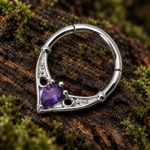 Puede incluir: Un anillo de segmento articulado en tono plateado con un frente decorativo en forma de V. El dise&ntilde;o incluye una piedra preciosa morada central con corte de pera, dos peque&ntilde;os recortes circulares y detalles de cuentas en el marco met&aacute;lico.