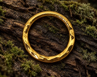 Pode incluir: Um anel circular de ouro com uma superfície texturizada e martelada com um acabamento irregular e reflexivo. O anel é uma banda contínua com um mecanismo de dobradiça visível, exibindo um brilho metálico polido e um padrão irregular.