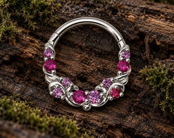 Pode incluir: Um anel circular de tom prateado com um segmento curvo decorativo adornado com várias pedras preciosas cor-de-rosa de corte redondo. O metal apresenta um padrão de espiral tipo videira que integra as pedras na metade inferior do aro.
