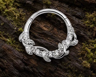 Pode incluir: Um anel circular de tom prateado com fecho de segmento articulado. O anel é adornado com um motivo decorativo de videira composto por folhas de metal polido e várias pedras pequenas, claras e de corte redondo ao longo da curva inferior.