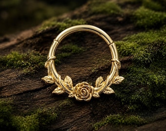 Puede incluir: Un anillo circular de tono dorado que presenta un motivo de rosa central flanqueado por delicadas hojas esculpidas a lo largo de la mitad inferior de la banda. La pieza de joyería tiene un acabado metálico pulido y un segmento articulado.