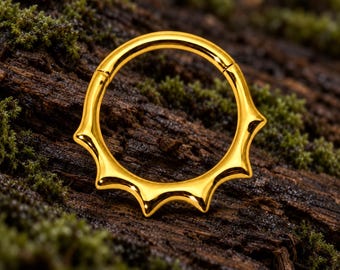 Pode incluir: Um anel de segmento articulado em tom dourado com um design de raios de sol, apresentando sete pontas que se estendem a partir da metade inferior do aro. A peça de joalharia tem uma superfície polida e refletora com um fecho seguro.