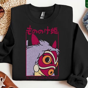 Puede incluir: Sudadera negra de cuello redondo con un gr&aacute;fico de un personaje de la pel&iacute;cula de animaci&oacute;n, La Princesa Mononoke. El dise&ntilde;o incluye una m&aacute;scara roja con detalles naranjas, pelo morado y texto japon&eacute;s. El texto "You cannot win against the forest spirit" est&aacute; en la parte inferior.