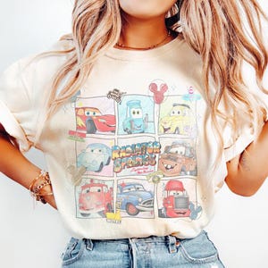 Puede incluir: Camiseta color crema con un gr&aacute;fico colorido de personajes de la pel&iacute;cula Cars. El dise&ntilde;o incluye varios coches en un estilo de c&oacute;mic, con las palabras "Radiator Springs" y "Lightning McQueen".