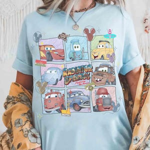 Puede incluir: Camiseta azul claro con un dise&ntilde;o de cuadr&iacute;cula de coches de dibujos animados de la pel&iacute;cula Cars. El dise&ntilde;o incluye a Rayo McQueen, Mate y otros personajes, con las palabras "Radiator Springs" y "Lightning McQueen".