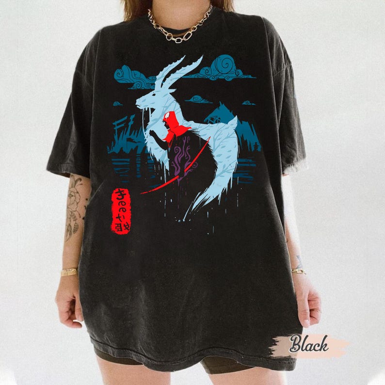 Może przedstawiać: Czarny t-shirt z wystylizowaną ilustracją stworzenia podobnego do jelenia z niebieskimi i czerwonymi akcentami, na tle g&oacute;r i chmur. Japoński tekst w czerwonym prostokącie.
