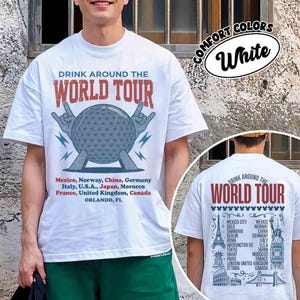 Könnte beinhalten: Ein weißes Kurzarm-T-Shirt mit einem Aufdruck, der den Text DRINK AROUND THE WORLD TOUR, eine geodätische Kuppel und eine Länderliste zeigt. Die Rückseite zeigt denselben Text mit Illustrationen globaler Wahrzeichen und Städtenamen.