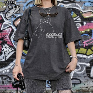 May include: Dark gray t-shirt featuring a white outline of a Studio Ghibli character with Japanese text. The shirt has short sleeves and a relaxed fit. The words "PEPPER" and "COMFORT COLORS" are printed at the top left.