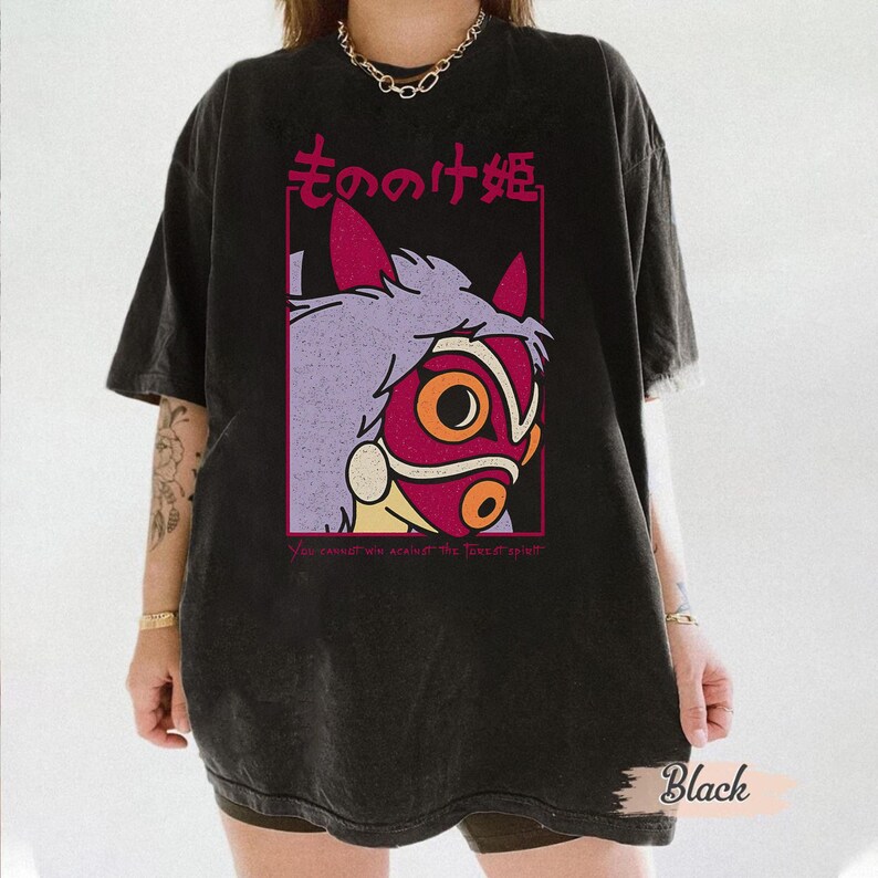 Puede incluir: Camiseta negra con un dise&ntilde;o gr&aacute;fico de un personaje de la pel&iacute;cula "La princesa Mononoke". El dise&ntilde;o incluye una cara estilizada con una m&aacute;scara roja, pelo morado y texto japon&eacute;s. Tambi&eacute;n incluye el texto "You cannot win against the forest spirit".