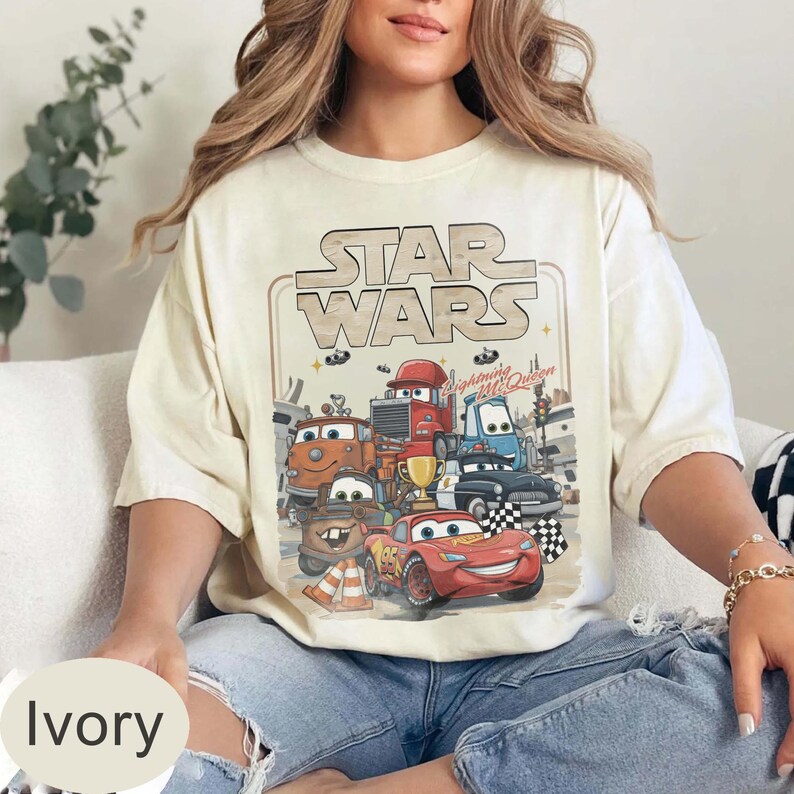 Puede incluir: Camiseta color marfil con un gr&aacute;fico de personajes de Cars y el texto "STAR WARS". El dise&ntilde;o incluye a Rayo McQueen y otros veh&iacute;culos. La camiseta es de corte holgado.