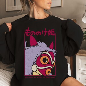 Puede incluir: Sudadera negra con un gr&aacute;fico de una m&aacute;scara con detalles en morado, rojo y naranja, y texto en japon&eacute;s. El texto "You cannot win against the forest spirit" est&aacute; impreso debajo.