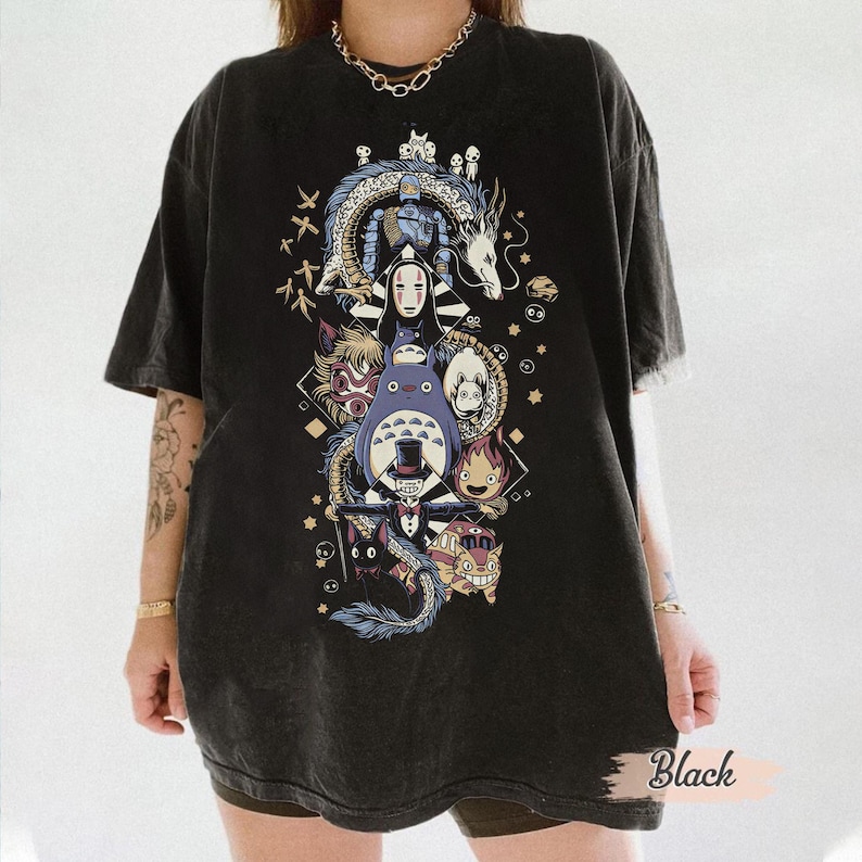 May include: Black t-shirt featuring a colorful graphic of anime characters, including a dragon, Totoro, and other figures. The design is centered on the shirt and includes Japanese text. The shirt has a washed, vintage look.