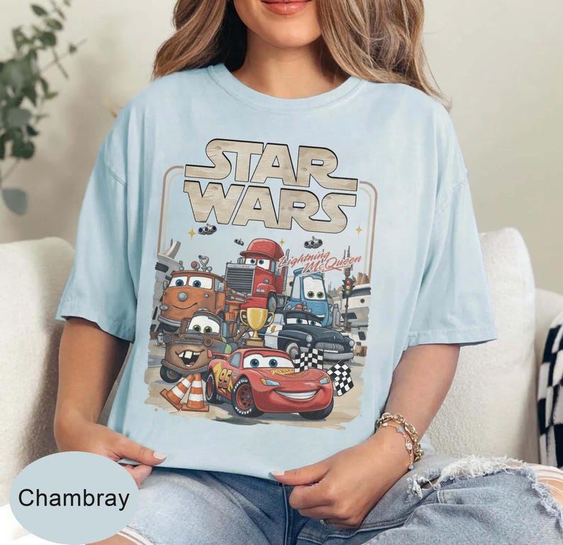 Puede incluir: Camiseta azul claro con un gr&aacute;fico de personajes de Cars y el logo de Star Wars. El dise&ntilde;o incluye a Rayo McQueen y otros veh&iacute;culos animados. La camiseta tiene la palabra "Chambray" en la parte inferior.