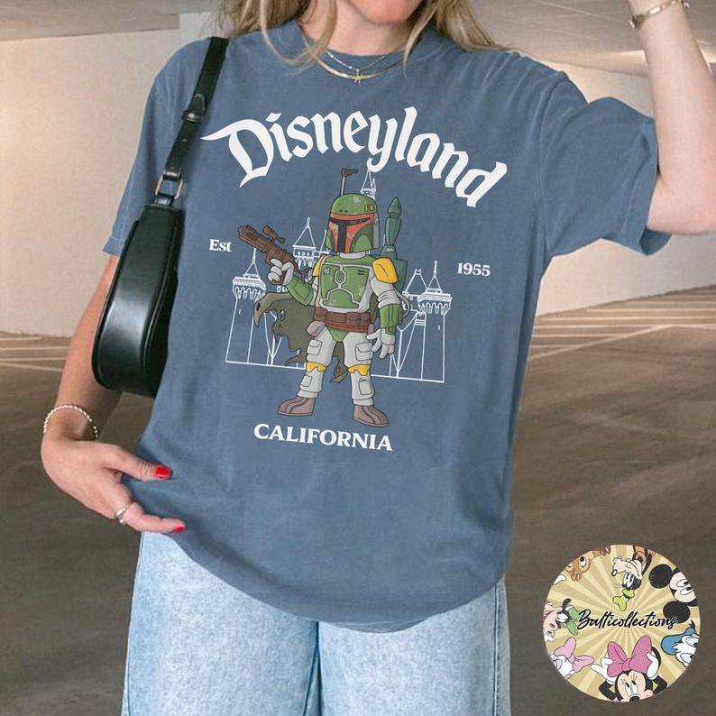 May include: Blue t-shirt featuring a Disneyland graphic with the text "Disneyland California 1955" and an illustration of Boba Fett. The shirt is a comfortable fit and has short sleeves.
