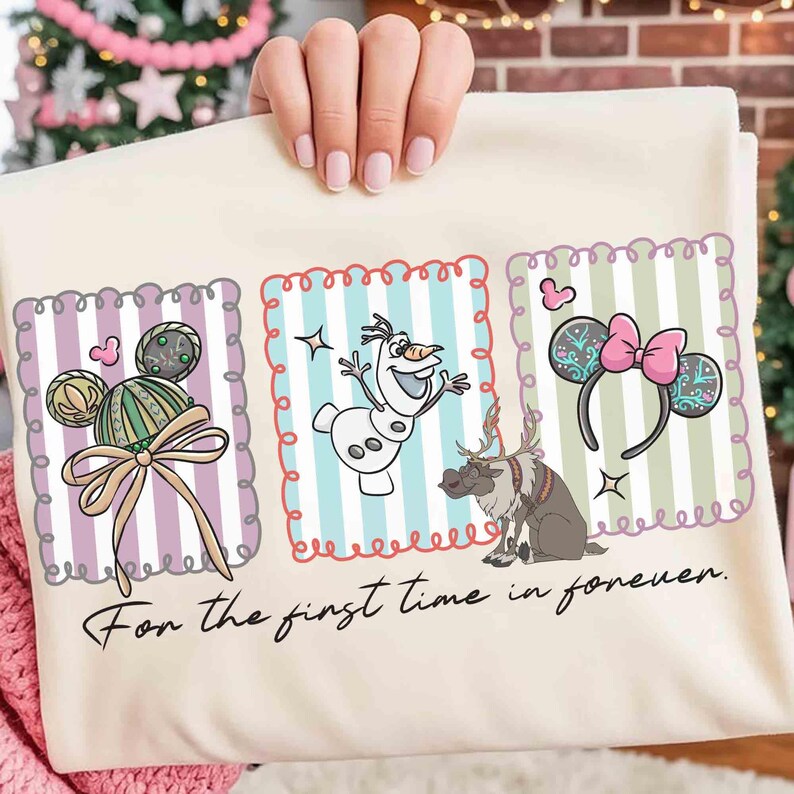 May include: Cream-colored t-shirt featuring three framed designs with Disney characters and accessories. The designs include Mickey Mouse ears, Olaf the snowman, reindeer, and Minnie Mouse ears. The text "For the first time in forever" is printed at the bottom.