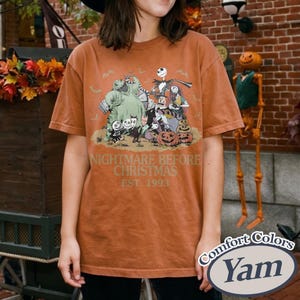 May include: A rust-colored short-sleeve t-shirt featuring a graphic print of characters from The Nightmare Before Christmas, including Jack Skellington, Sally, and Oogie Boogie, with the text Nightmare Before Christmas Est. 1993 printed below.