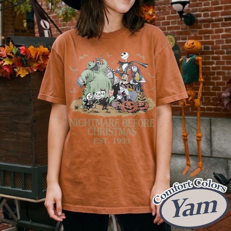 May include: A rust-colored short-sleeve t-shirt featuring a graphic print of characters from The Nightmare Before Christmas, including Jack Skellington, Sally, and Oogie Boogie, with the text Nightmare Before Christmas Est. 1993 printed below.