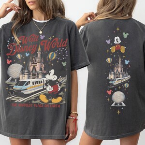 Pu&ograve; includere: Una t-shirt grigio antracite con una stampa grafica di Topolino, una monorotaia, un castello e la sfera di Epcot. Il davanti mostra il testo Walt Disney World e The Happiest Place On Earth. Il retro presenta una disposizione verticale delle icone.