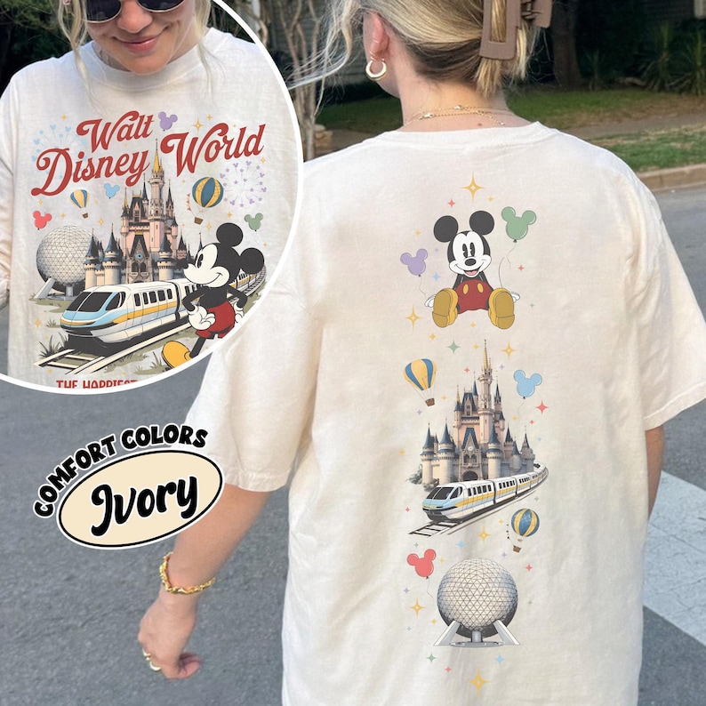 Pu&ograve; includere: Una t-shirt color avorio con una stampa grafica verticale di Topolino, un castello, una monorotaia e una cupola geodetica, arricchita da palloncini e stelle colorati. Il testo Walt Disney World &egrave; stampato in rosso sopra l'illustrazione del castello.