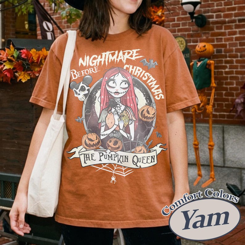 Pu&ograve; includere: Una maglietta marrone con una grafica di "Nightmare Before Christmas". Il design include Sally, zucche e la scritta "The Pumpkin Queen". La maglietta &egrave; del marchio Comfort Colors nel colore "Yam".