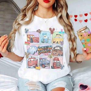Puede incluir: Camiseta blanca con una colorida cuadr&iacute;cula de personajes de la pel&iacute;cula Cars. El dise&ntilde;o incluye a Rayo McQueen, Mate y otros personajes de Radiator Springs. La camiseta tiene cuello redondo y mangas cortas, perfecta para uso casual.