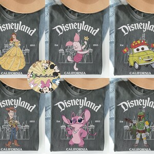 May include: A collection of gray t-shirts featuring Disneyland graphics. Each shirt displays a different character, including Belle, Piglet, Mater, Woody, Stitch, and Boba Fett. The Disneyland logo and "California" are printed on each shirt.