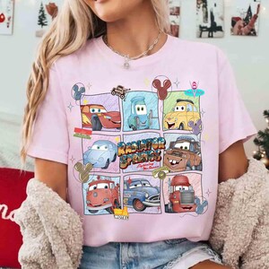 Puede incluir: Camiseta rosa claro con un dise&ntilde;o gr&aacute;fico colorido de personajes de la pel&iacute;cula Cars. El dise&ntilde;o incluye im&aacute;genes de varios coches y el texto "Radiator Springs". La camiseta tiene cuello redondo y mangas cortas.