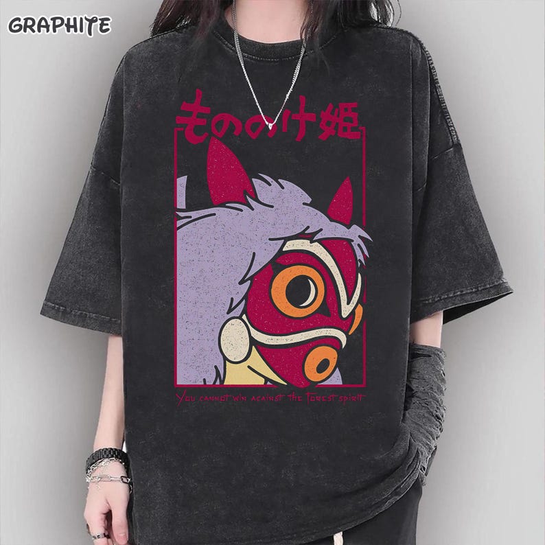 Puede incluir: Camiseta de color grafito con un gr&aacute;fico de una m&aacute;scara roja y naranja con detalles en morado y amarillo, y texto japon&eacute;s. La camiseta tambi&eacute;n tiene el texto "You cannot win against the forest spirit."