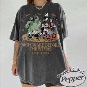 May include: A charcoal gray short-sleeve t-shirt featuring a graphic print of characters from The Nightmare Before Christmas, including Jack Skellington, Sally, and Oogie Boogie, with the text Nightmare Before Christmas Est. 1993 printed below.
