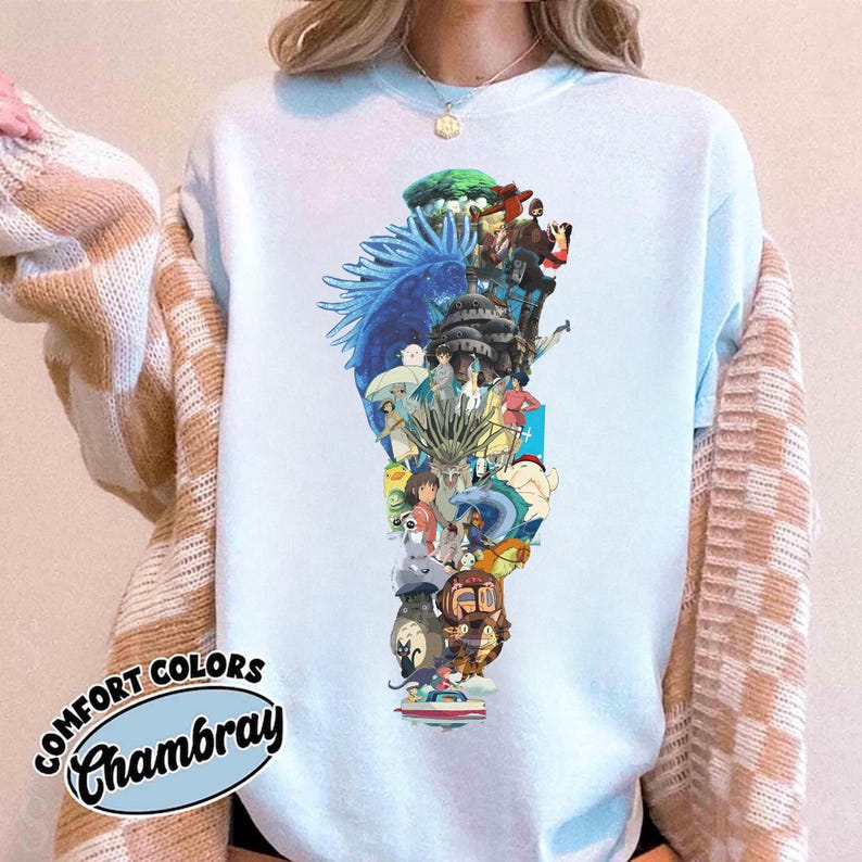May include: Light blue sweatshirt featuring a colorful graphic design of various anime characters. The design includes a blue dragon, forest, and several figures. The sweatshirt has the text "Comfort Colors Chambray" in a circular design.