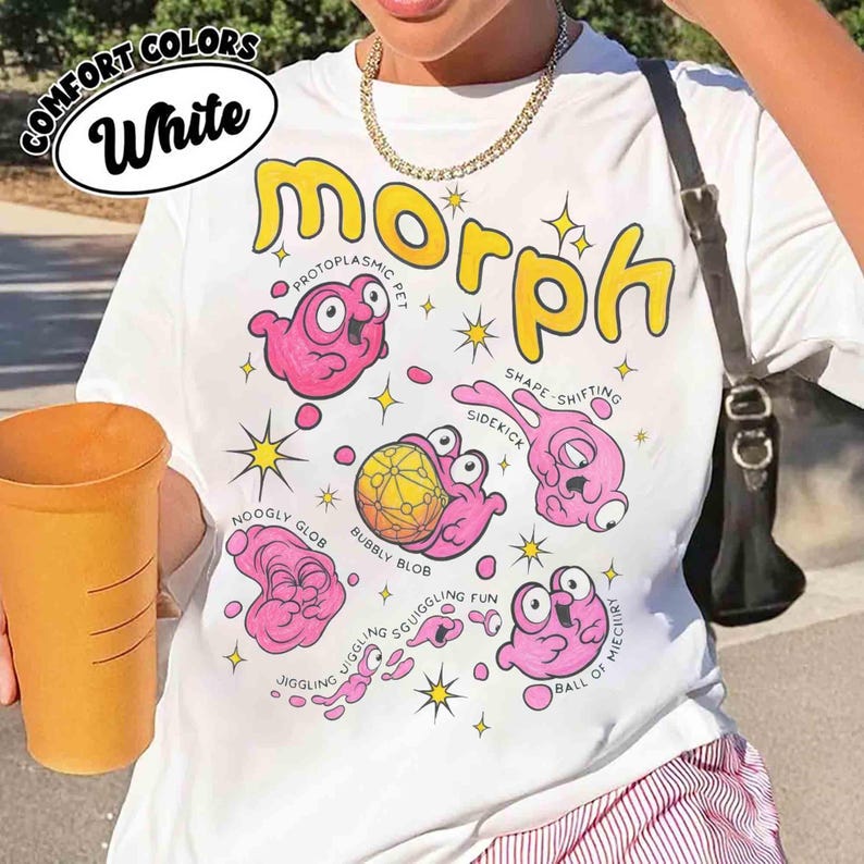 May include: White t-shirt featuring a cartoon design of pink blob creatures and the word "morph" in yellow. The shirt includes text like "Protoplasmic Pet" and "Shape-shifting Sidekick". The shirt is labeled "Comfort Colors".
