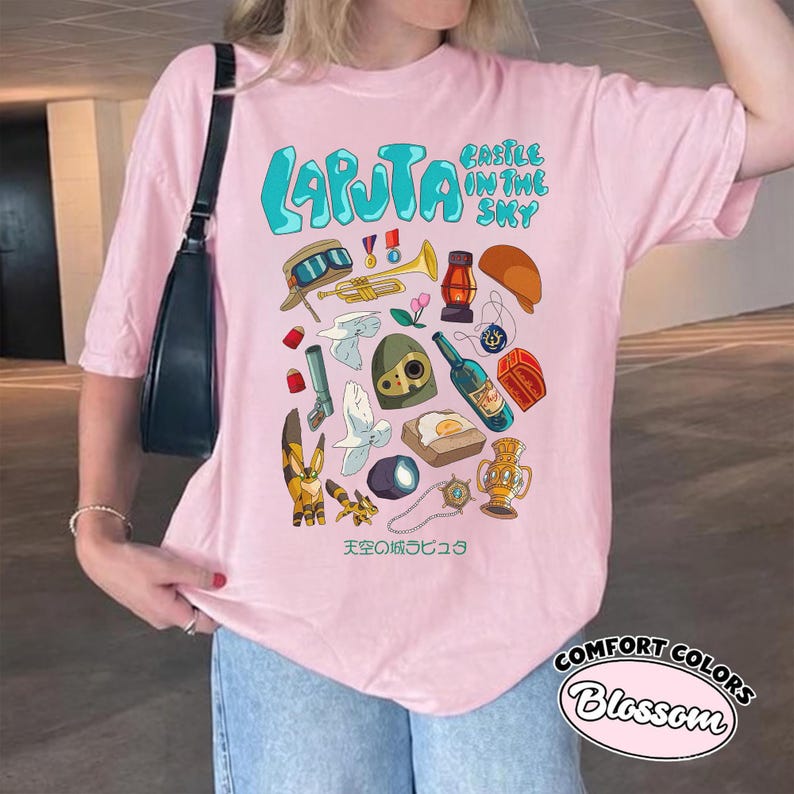 May include: Pink t-shirt with a graphic featuring the text "Laputa Castle in the Sky" in turquoise, along with various illustrations. The shirt also has the text "Comfort Colors Blossom" in a circular design.