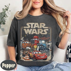 Puede incluir: Camiseta gris oscuro con un dise&ntilde;o de personajes de la pel&iacute;cula "Cars" y el texto "Star Wars". El dise&ntilde;o incluye a Rayo McQueen y otros veh&iacute;culos. La camiseta tiene un aspecto vintage y desgastado.