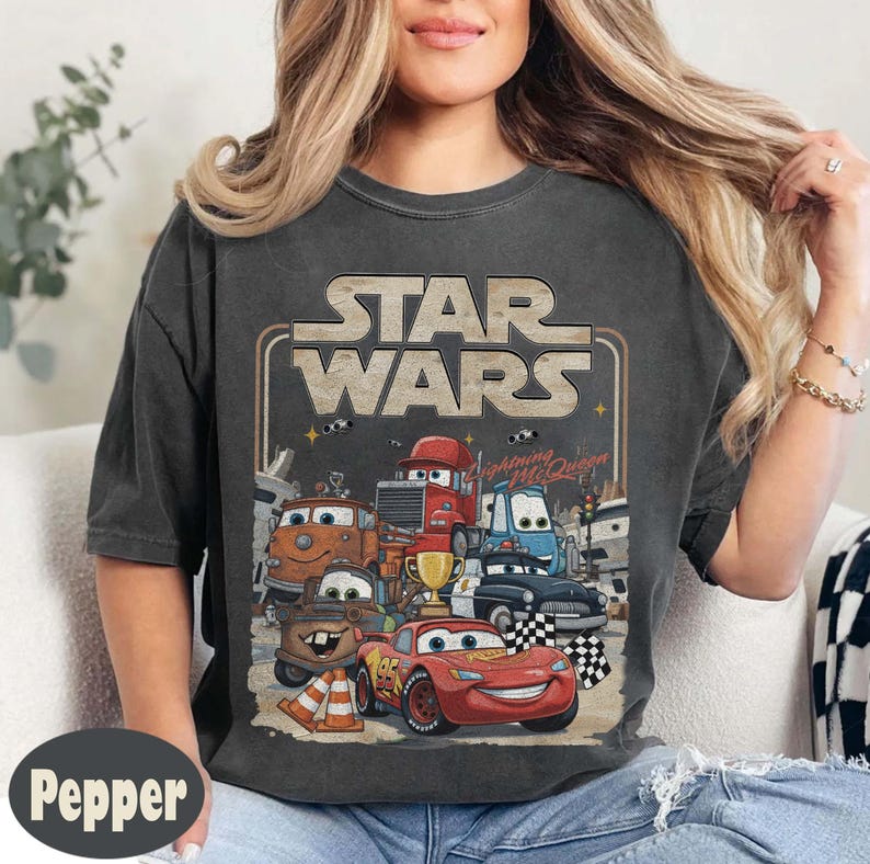 Puede incluir: Camiseta gris oscuro con un dise&ntilde;o de personajes de la pel&iacute;cula "Cars" y el texto "Star Wars". El dise&ntilde;o incluye a Rayo McQueen y otros veh&iacute;culos. La camiseta tiene un aspecto vintage y desgastado.
