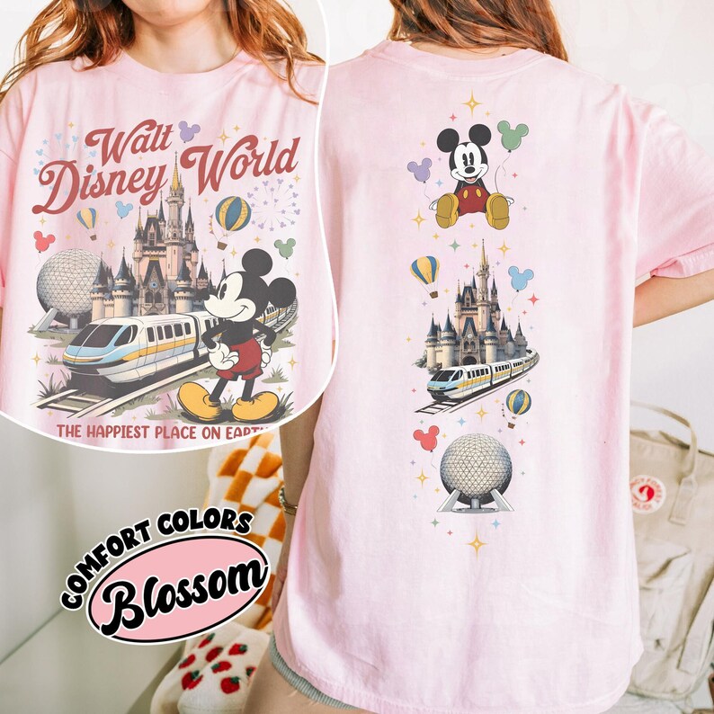 Pu&ograve; includere: Una t-shirt rosa chiaro con una stampa grafica di Walt Disney World, che include il castello, la monorotaia, la sfera di Epcot e Topolino. Il testo recita Walt Disney World e The Happiest Place on Earth, con stelle e palloncini colorati.