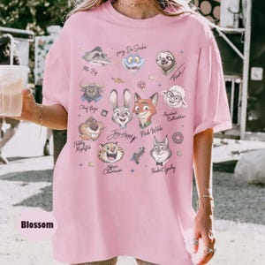 May include: A light pink oversized t-shirt featuring cartoon illustrations of characters from a movie. The shirt includes the text "Joy Hopps" and "Nick Wilde". The word "Blossom" is printed at the bottom.