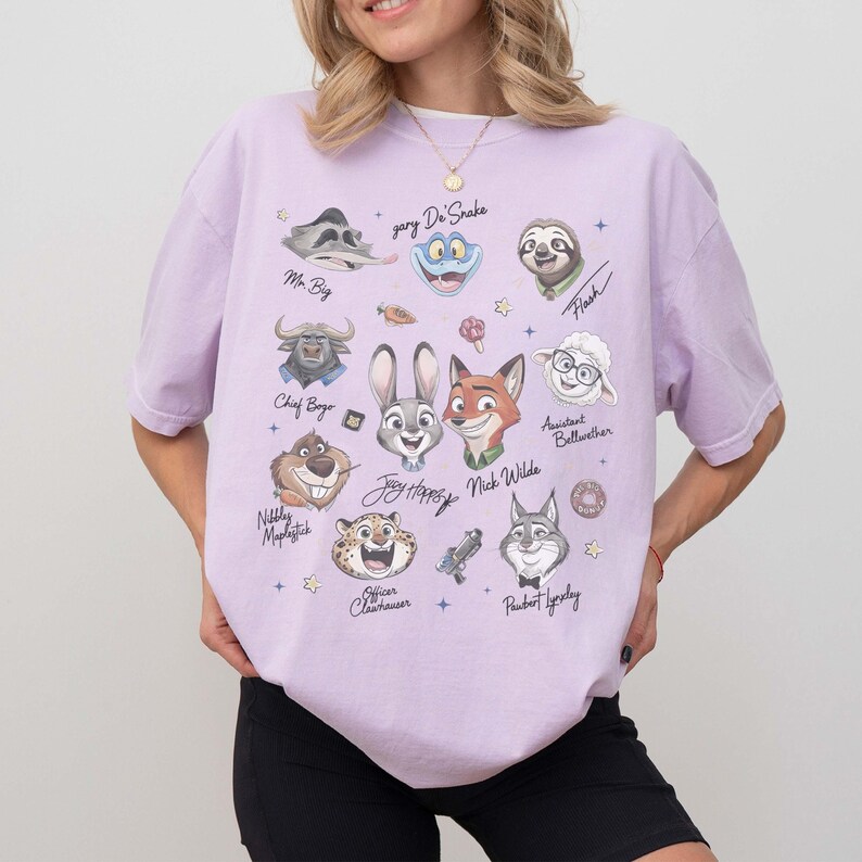 May include: A light purple t-shirt featuring cartoon characters from a movie. The shirt has illustrations of a bunny, fox, sloth, and other characters. The names of the characters are written below them.