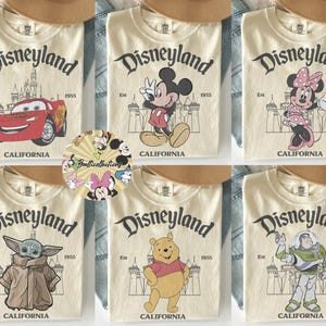 May include: Cream-colored t-shirts featuring Disneyland graphics. Designs include Lightning McQueen, Mickey Mouse, Minnie Mouse, Grogu, Winnie the Pooh, and Buzz Lightyear. Each shirt has the Disneyland logo and "California" printed on it.