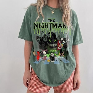 May include: Green t-shirt featuring a graphic from "The Nightmare Before Christmas." The design includes characters like Jack Skellington and Sally, with the title in dripping green letters. The shirt is paired with red and white checkered shorts.