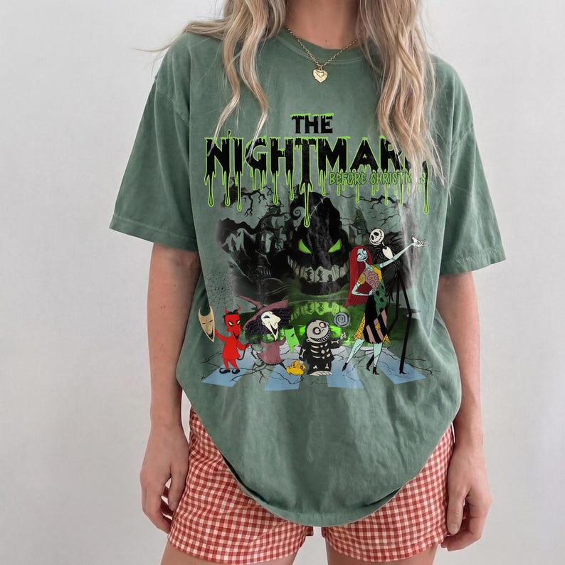 May include: Green t-shirt featuring a graphic from "The Nightmare Before Christmas." The design includes characters like Jack Skellington and Sally, with the title in dripping green letters. The shirt is paired with red and white checkered shorts.